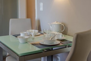 A dining table with white tableware and a teapot, set in a room with a light-colored wall and a chair. - Margarethenstraße Holiday Apartment 10 (Sylt\/Westerland)