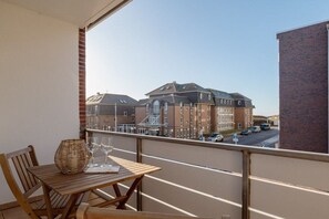 A balcony with a wooden table and chairs, overlooking a street with buildings. - Margarethenstraße Holiday Apartment 10 (Sylt\/Westerland)
