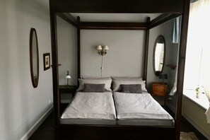 Ein Himmelbett mit dunklem Gestell, zwei Nachttische, eine Wandlampe und ein Spiegel.