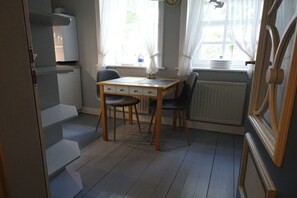 Eine kleine Küche mit Tisch und Stühlen, einem Fenster mit Vorhängen und einer Heizung.