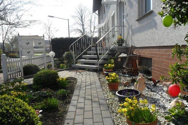 A pathway leading to a building with a white fence, potted plants, and a brick wall. - Holiday apartment with 1 bedroom (Wunstorf\/ Steinhude)