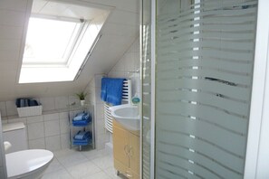 A modern bathroom with a skylight, a white sink, a glass shower enclosure, and a towel rack with blue towels. - Holiday apartment with 1 bedroom (Wunstorf\/ Steinhude)