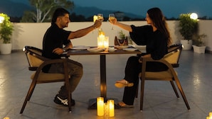 Two people seated at an outdoor table with candles, surrounded by potted plants.