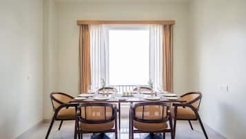 Un comedor con una mesa dispuesta para seis personas, rodeada de sillas de mimbre, un ventanal con cortinas y vistas al exterior.
