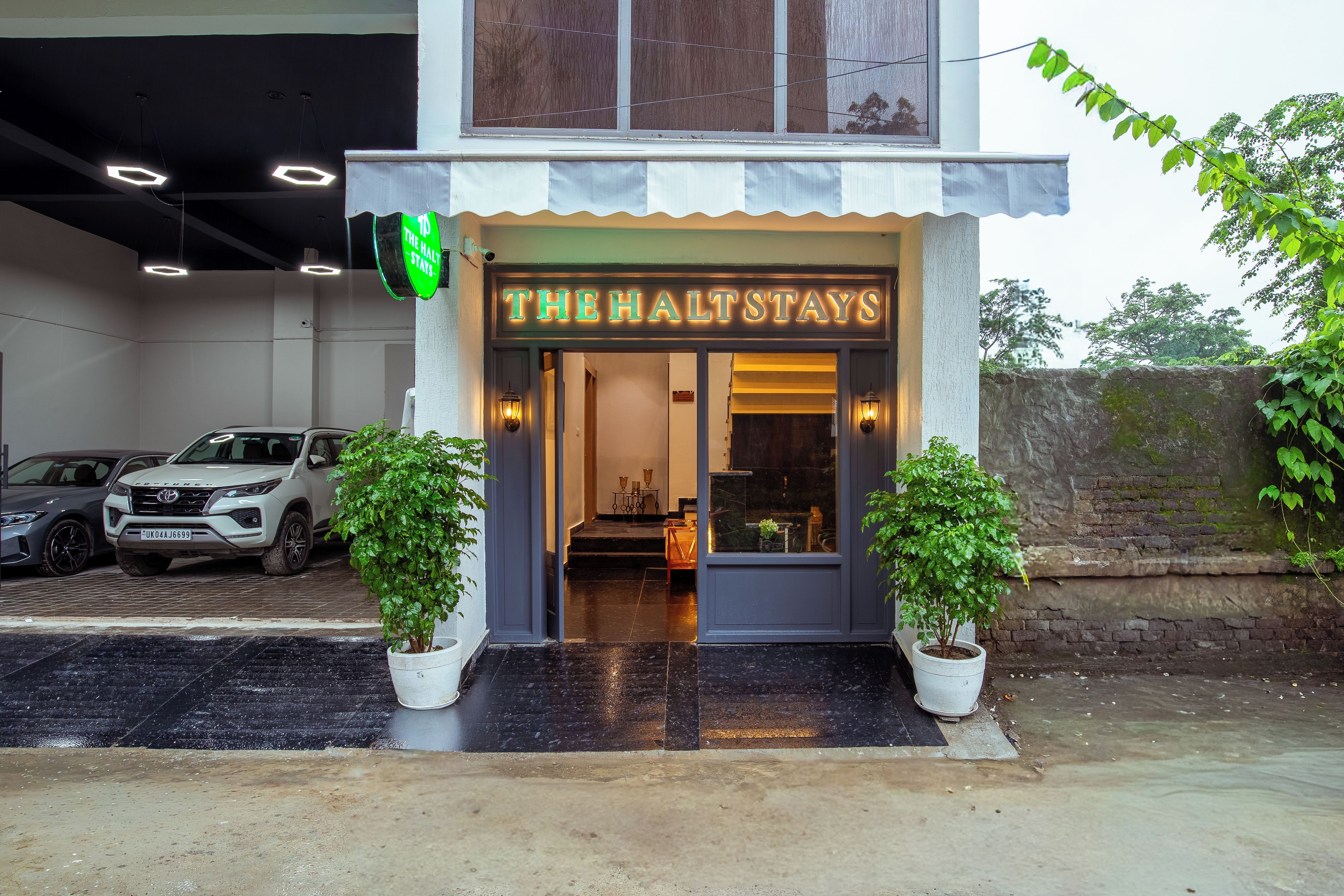 En hotelindgang med et skilt, der viser 'THE HALTSTAYS', og to krukkeplanter på hver side.