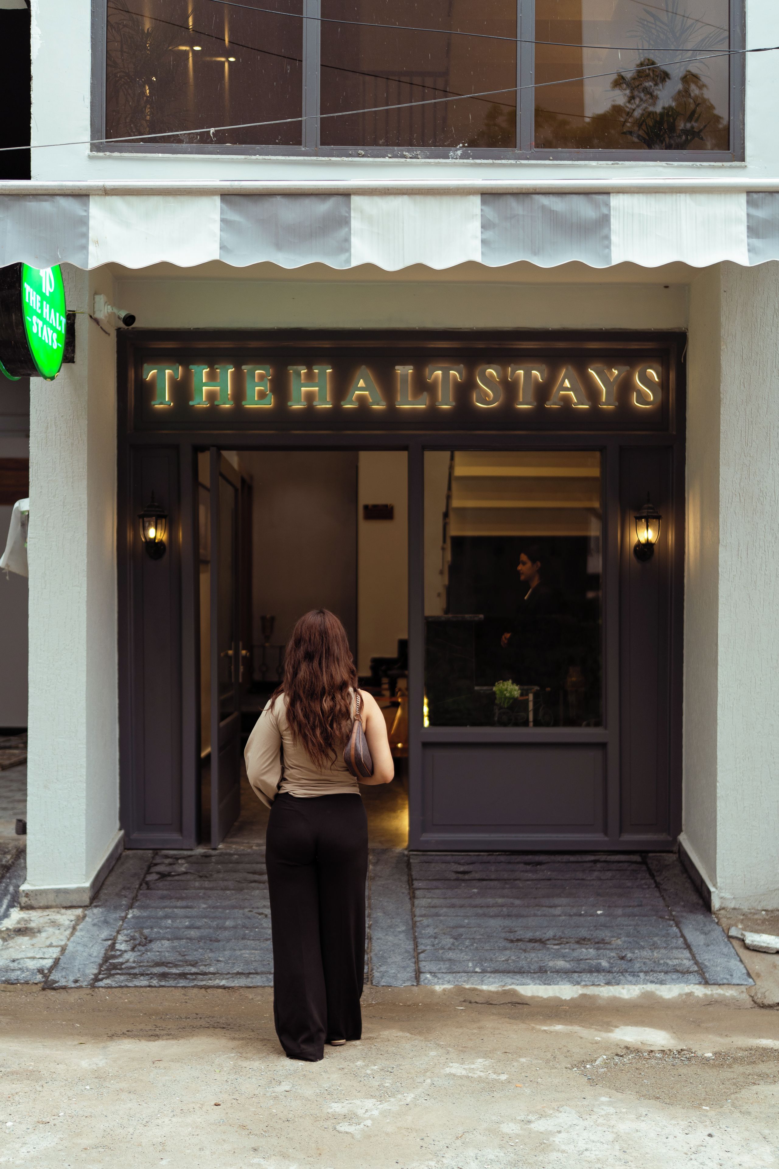 A hotel entrance with a neon sign reading 'THE HALTSTAYS' and a visible entrance door.