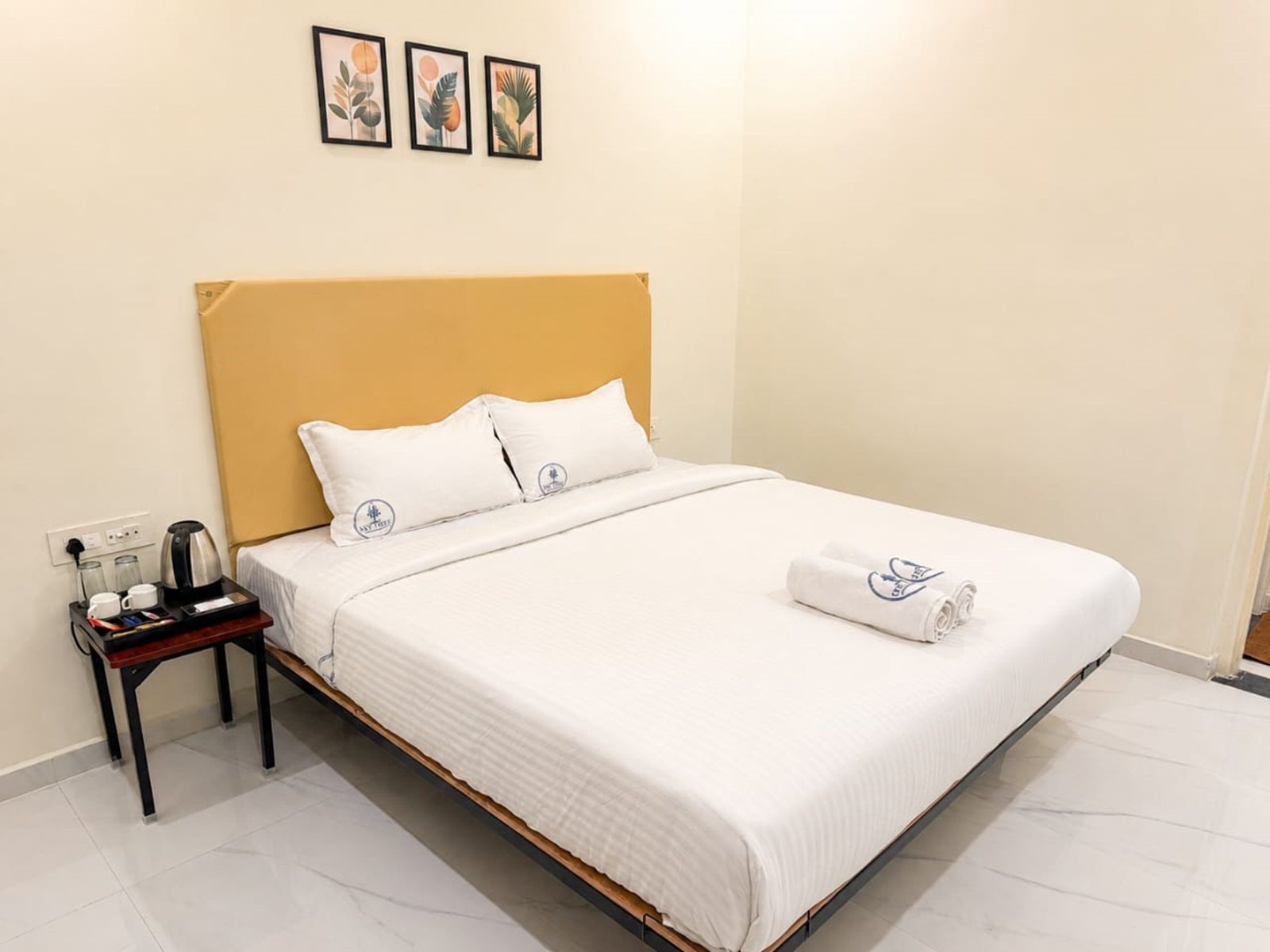 Una habitación de hotel con cama, mesita de noche, cafetera y toalla.