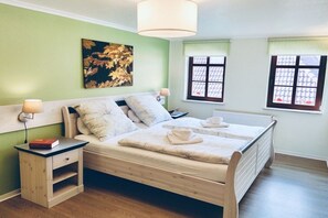 Un dormitorio ordenado con cama, mesitas de noche, lámpara y ventana con vistas.