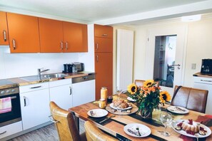 Eine moderne Küche mit weißen Schränken, einem Holzespeisetisch für vier Personen und einer Vase mit Sonnenblumen.