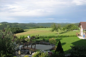 A garden with a pond, a wooden deck, and a view of rolling hills. - at the Eifel National Park (Nideggen)