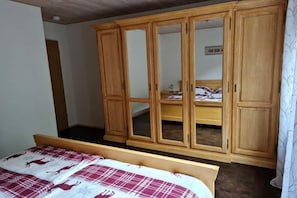 A bedroom with a wooden wardrobe, a bed with a checkered bedspread, and a mirror above the bed. - at the Eifel National Park (Nideggen)