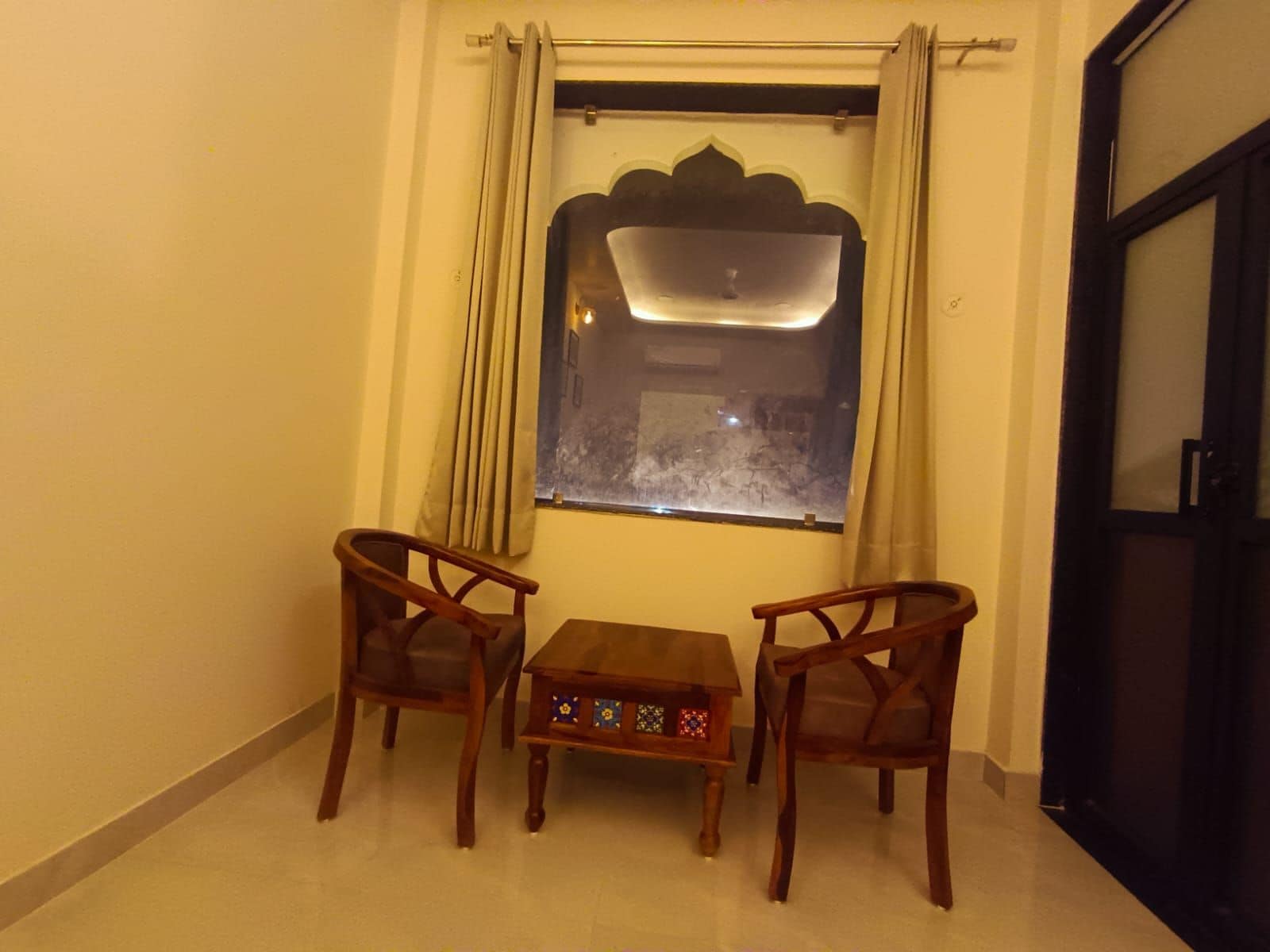 Ein Zimmer mit zwei hölzernen Stühlen und einem kleinen Tisch, einem Fenster mit Vorhängen und einer Tür.