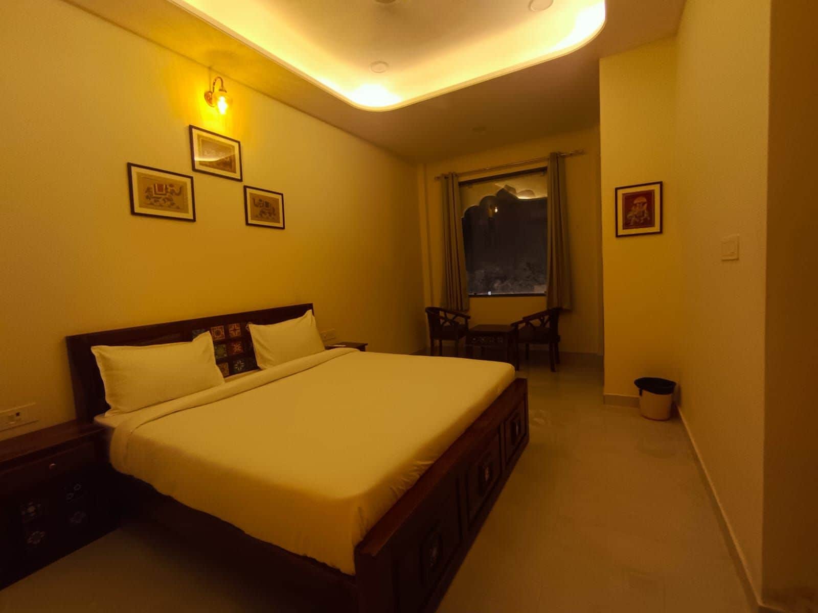 Una habitación de hotel con una cama grande, una mesita pequeña, dos sillas, una ventana con vistas y varias fotografías enmarcadas en las paredes.