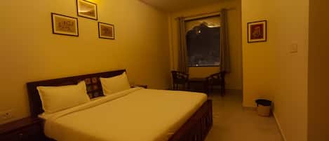 Una habitación de hotel con una cama grande, una mesita pequeña, dos sillas, una ventana con vistas y varias fotografías enmarcadas en las paredes.
