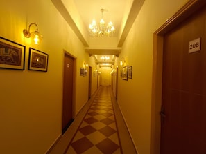 Un pasillo de hotel con piso de cuadros, lámparas fijadas en la pared y un candelabro.