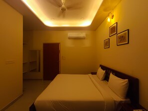 Une chambre d’hôtel équipée d’un lit, d’un ventilateur de plafond, d’un appareil de climatisation et d’une porte donnant sur un couloir.