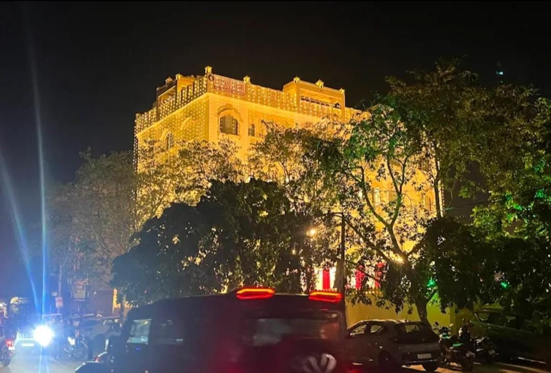 Un edificio con una entrada destacada y un balcón, rodeado de árboles y vehículos.