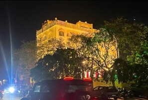 Un edificio con una entrada destacada y un balcón, rodeado de árboles y vehículos.