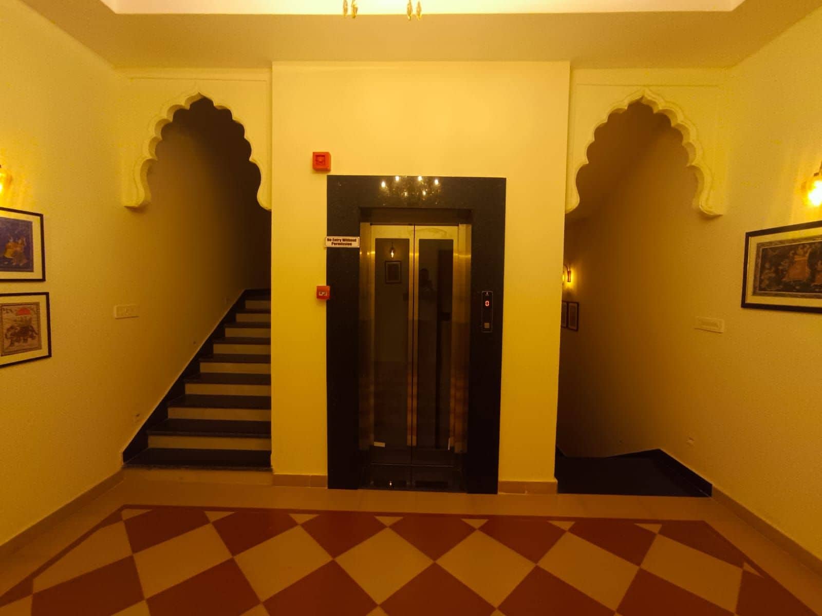Eine Hotelhalle mit Treppe, Aufzug und einem gemusterten Boden.