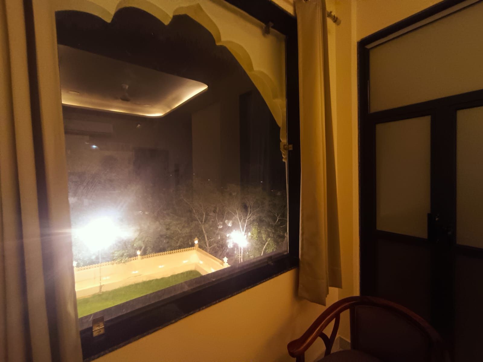 Habitación con un amplio ventanal que da a un espacio exterior bien iluminado, una puerta y una silla.