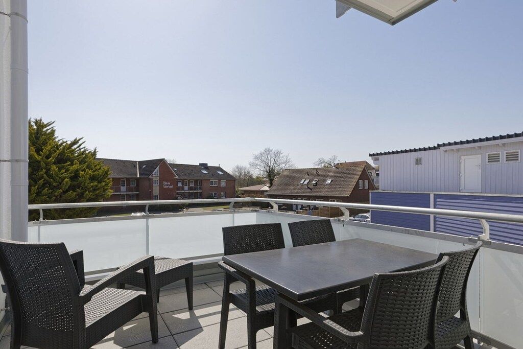 Ein Balkon mit Tisch und Stühlen, der auf einen Wohnbereich mit Häusern und einem blauen Gebäude blickt.