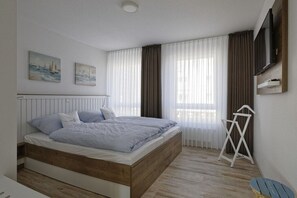 A bedroom with a bed, a TV mounted on the wall, and a window with curtains. - Holiday apartment with 1 bedroom (Cuxhaven)