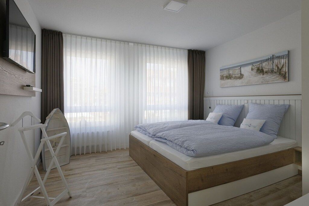 A bedroom with a bed, a TV, a painting, and a window with curtains.