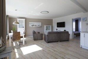 A modern living room with a sofa, a dining table, and a TV mounted on the wall. - Holiday apartment with 1 bedroom (Cuxhaven)