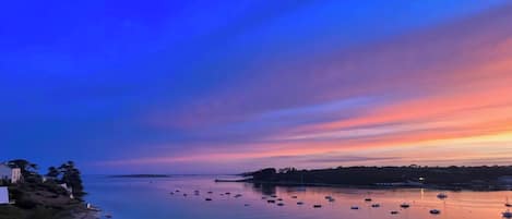 A coastal scene with boats anchored in calm waters, a clear sky, and a shoreline with buildings.