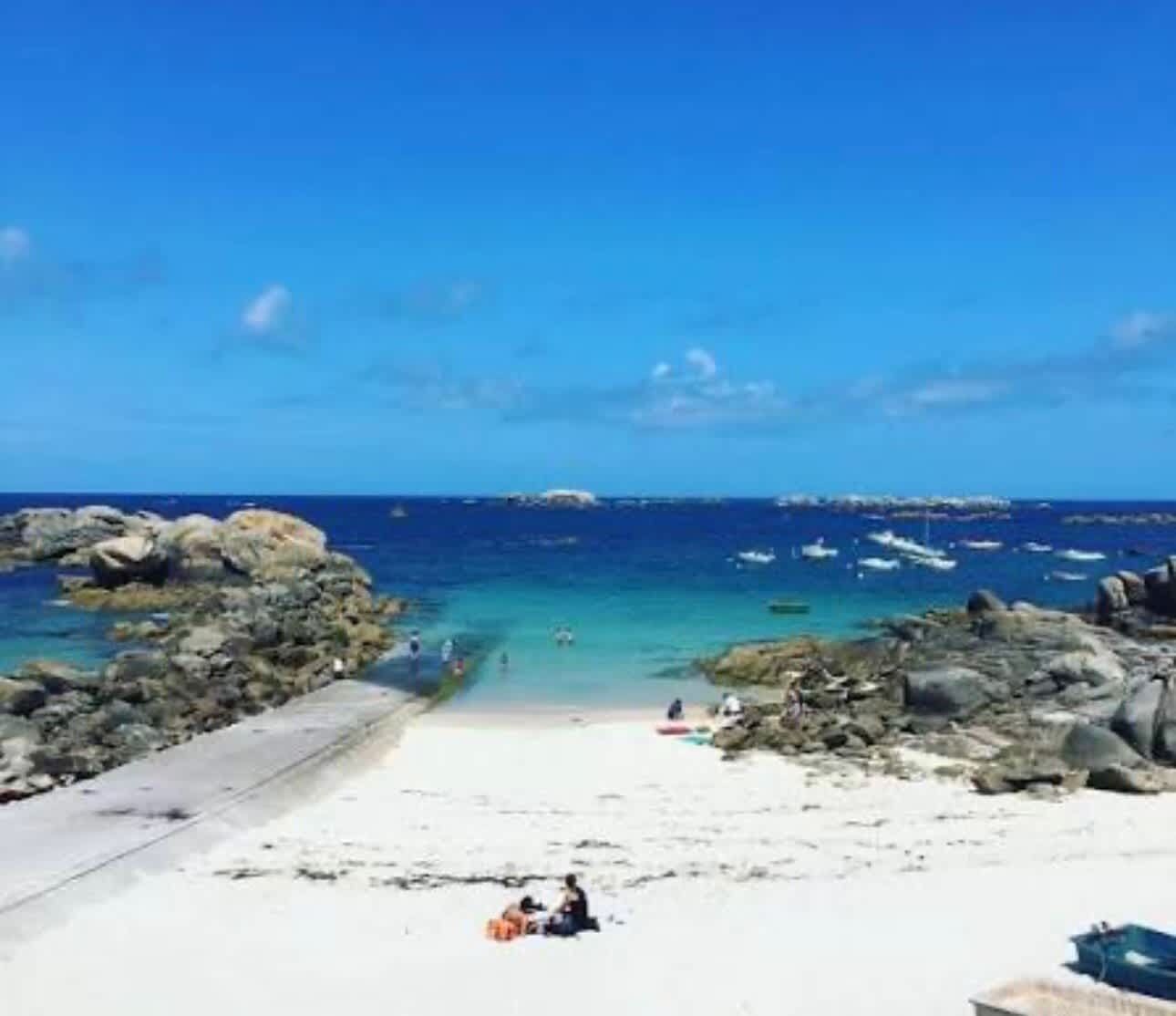 Una playa con aguas azul turquesa, zonas rocosas y una orilla arenosa.