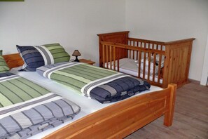Ein Zimmer mit zwei Holzbetten, jeweils mit Matratze und Kissen, sowie einem hölzernen Wiege.