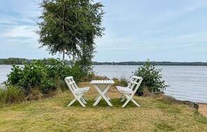 Eine Uferlandschaft mit Tisch und zwei Stühlen, umgeben von Grün und Blick auf das Wasser.