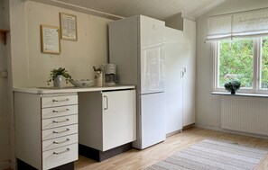 Eine Küche mit einem weißen Kühlschrank, einer Kaffeemaschine und einem Fenster mit Blick ins Grüne.