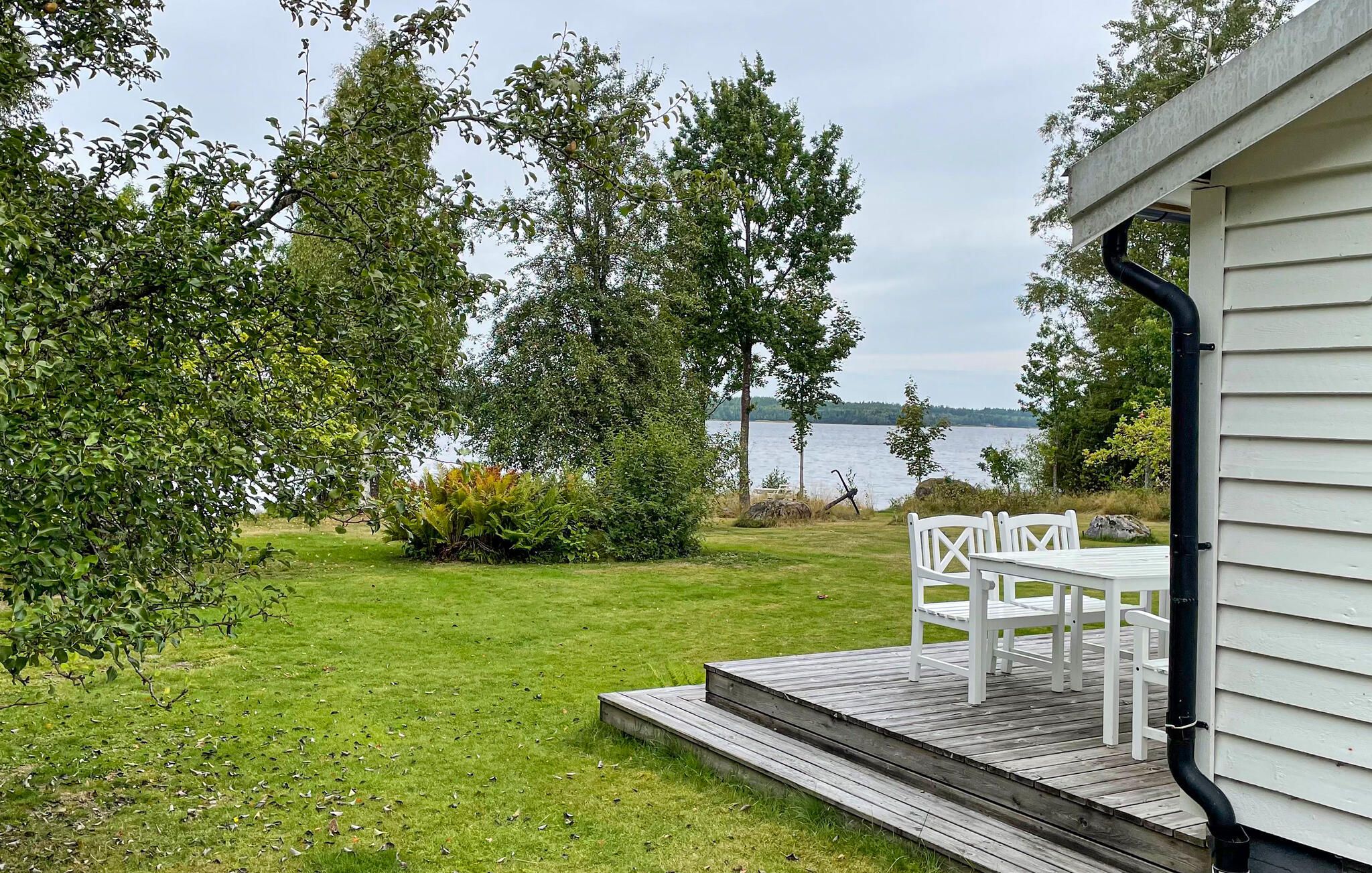 A deck with white chairs overlooking a lake, surrounded by greenery and trees.