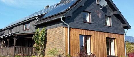 A two-story house with a sloped roof, solar panels, and a satellite dish.