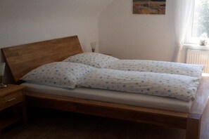 A double bed with a wooden headboard and floral bedding, a bedside table, and a window with curtains. - Holiday apartment in Monschau with barbecue (Monschau)