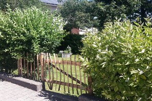 A wooden fence with a gate, surrounded by lush green shrubs and trees. - Holiday apartment in Monschau with barbecue (Monschau)