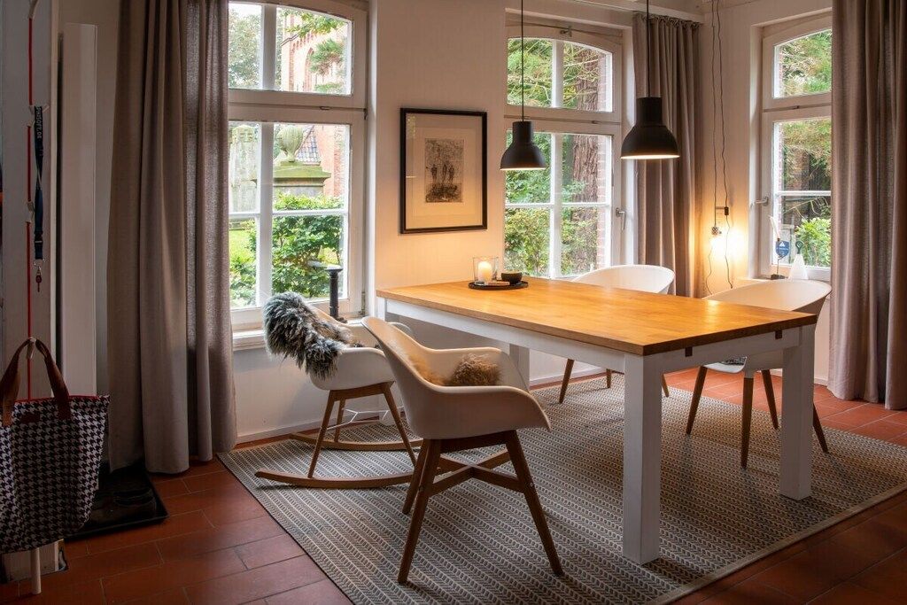 A dining area with a wooden table, white chairs, and a view through large windows.