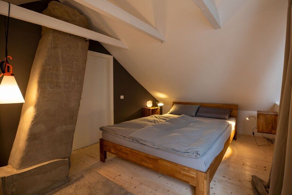 A bedroom with a sloped ceiling, a wooden bed, and two bedside lamps.