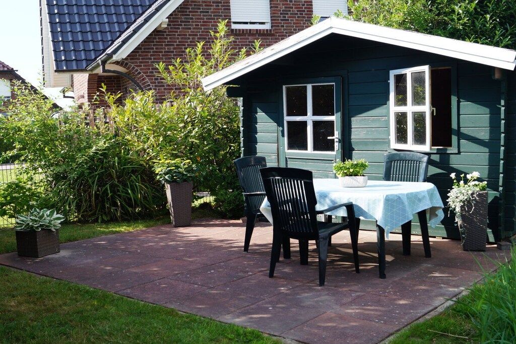 A patio with a table and chairs, surrounded by greenery and a house in the background.