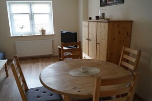 Ein Zimmer mit einem runden Holztisch, vier Stühlen, einem Fernseher auf einem Schrank, einem Schrank und einem Fenster mit Jalousien.