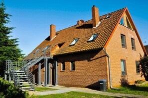 A brick building with a sloped roof, a staircase leading to an upper level, and a small trash bin. - Holiday apartment with 3 bedrooms (Neustadt)