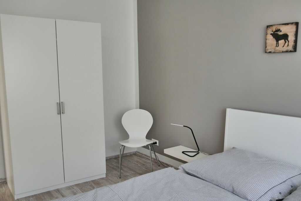 Ein Schlafzimmer mit einem Bett, einem weißen Wandschrank, einem weißen Sessel, einem Nachttisch und einem an der Wand hängenden Bild von einem Elch.