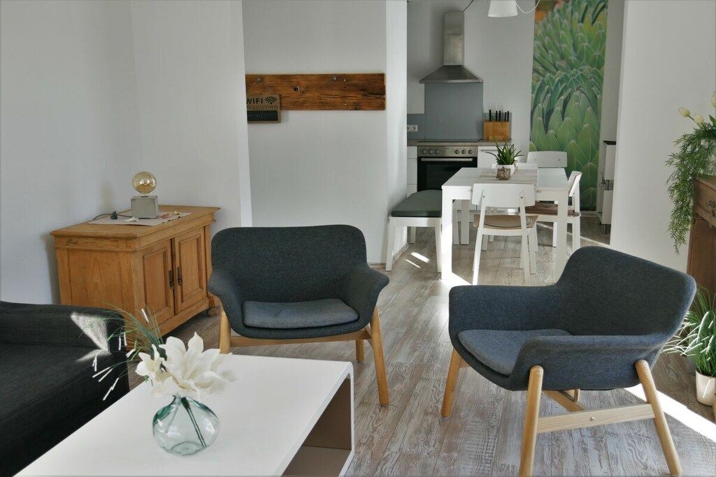Un salon moderne comprenant un canapé, deux fauteuils, une table basse avec un vase, et un coin repas avec une table et des chaises.