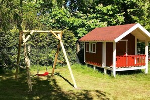 A wooden swing set and a small red-roofed cabin with a porch, surrounded by greenery. - Holiday apartment with 3 bedrooms (Neustadt)