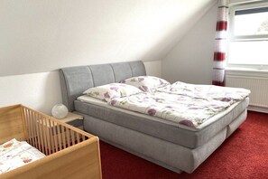 A bedroom with a single bed, a crib, and a window with curtains. - Holiday apartment in Scharbeutz with Wi-Fi (Scharbeutz)