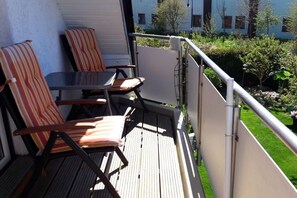 A balcony with two chairs and a table, a metal railing, and a view of a green garden and buildings in the background. - Holiday apartment in Scharbeutz with Wi-Fi (Scharbeutz)