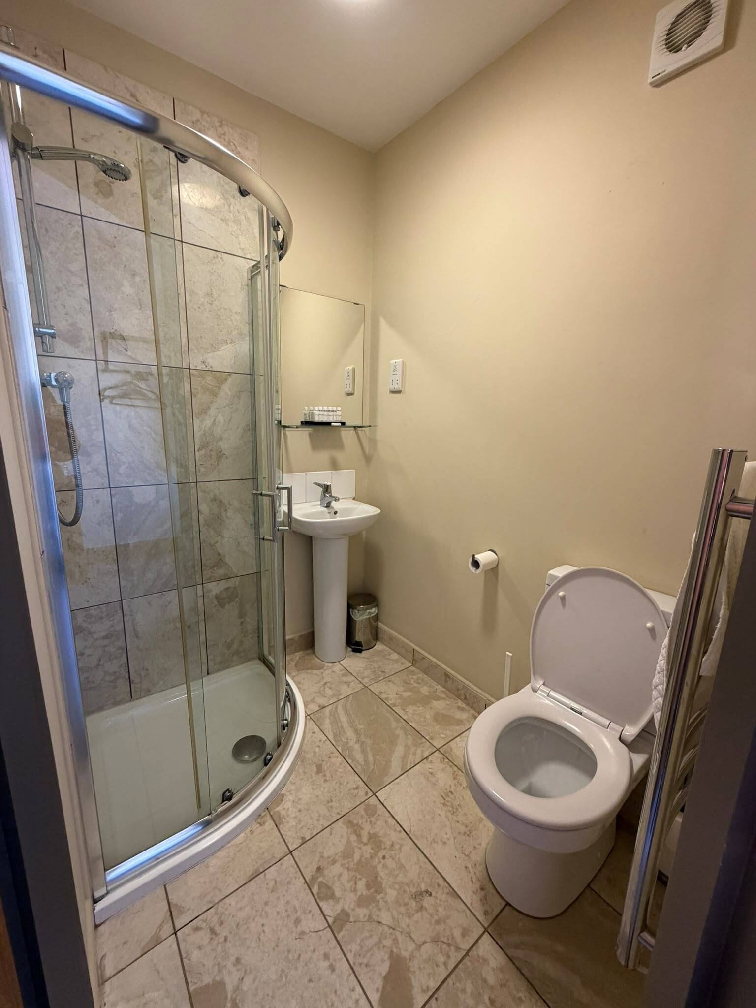 A bathroom with a glass-enclosed shower, a pedestal sink, and a toilet.