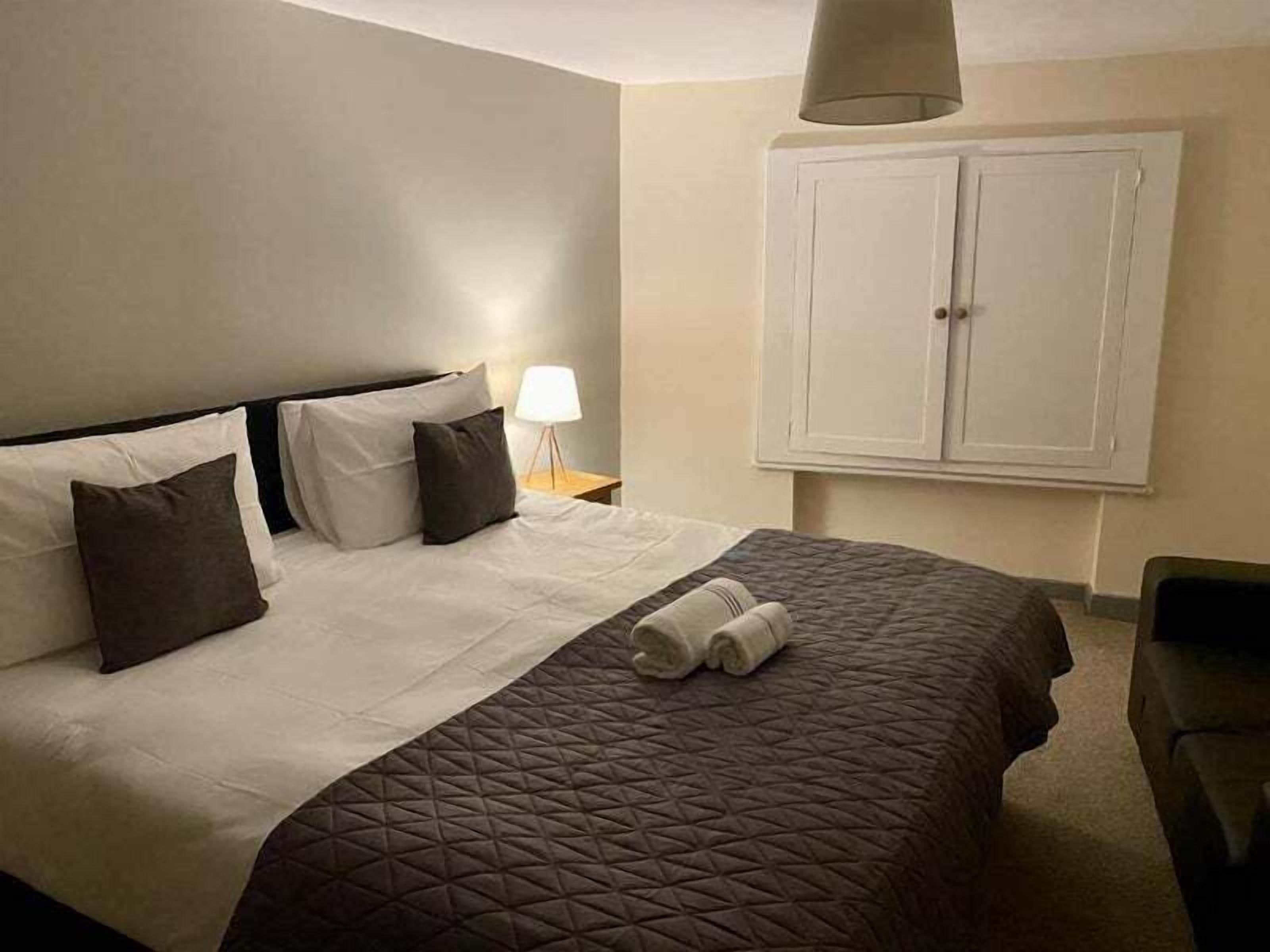Una habitación de hotel con una cama, una mesita de noche, una lámpara y un armario.