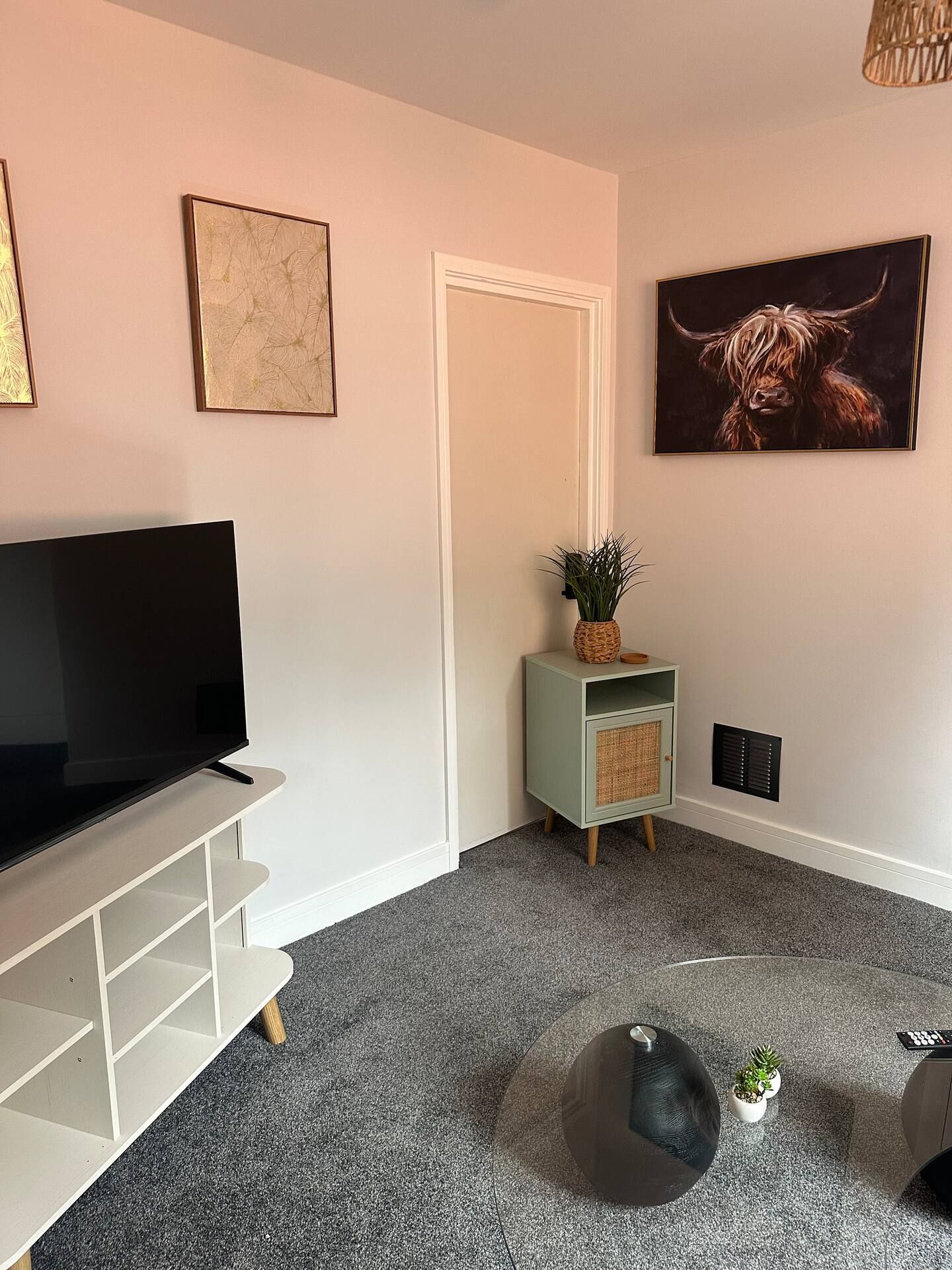 A living room with a flat-screen TV, a green cabinet with a plant, and a large painting of a bull.